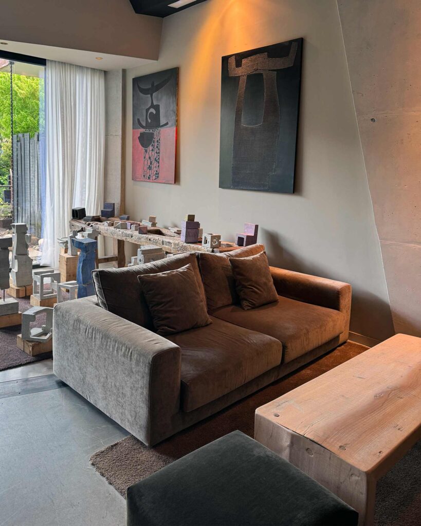 Modern lounge with brown sofa, abstract wall art and sculptural objects arranged on a long wooden table.