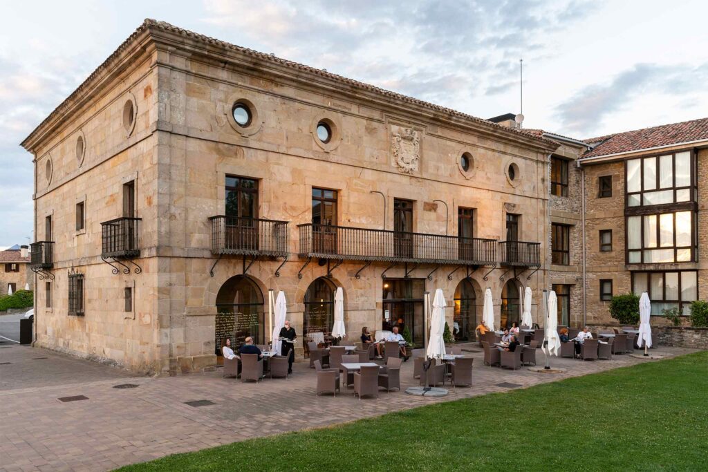 Historic stone manor hotel with wrought-iron balconies and a spacious terrace where guests dine outdoors.