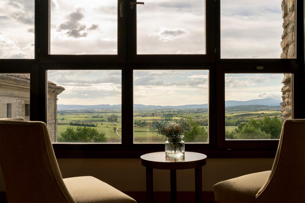 Comfortable seating area at Parador de Argómaniz beside large windows framing sweeping views of green fields and distant hills.