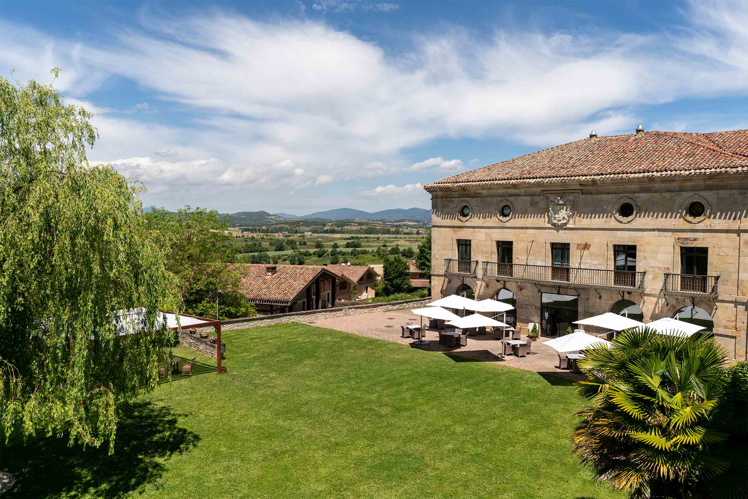Historic countryside hotel surrounded by landscaped gardens and terrace seating overlooking the Basque landscape.