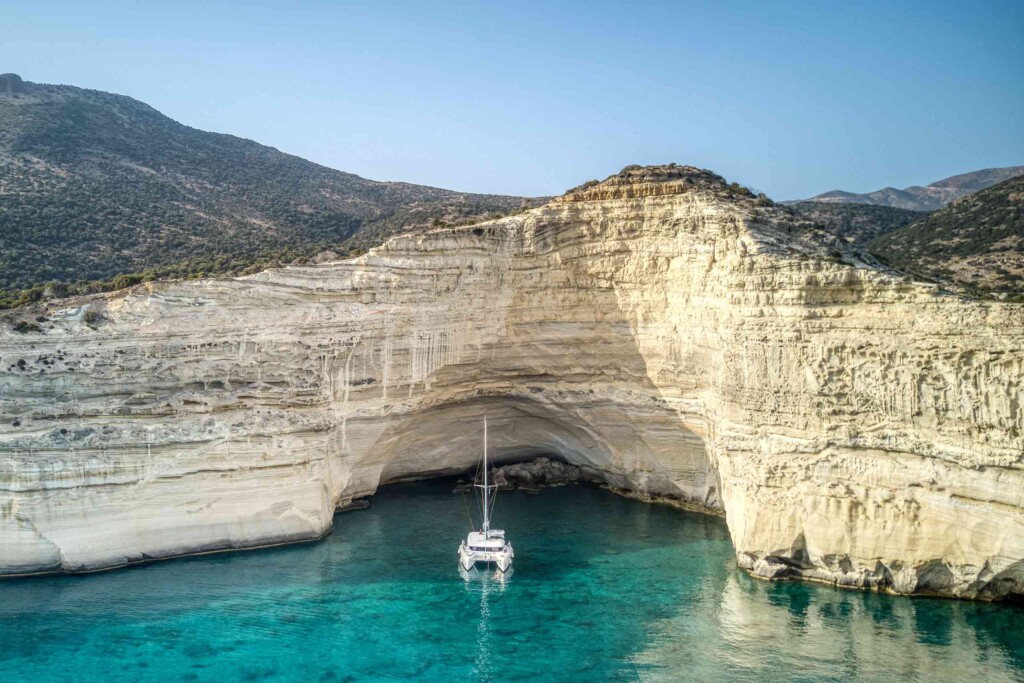Catamaran on the turquoise Aegean sea, flanking the dramatic white cliffs of Milos in Greece – summer travel with Scott Dunn
