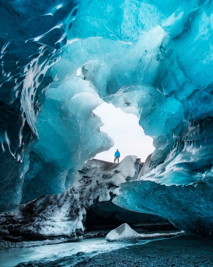 A man in a blue jacket looks into a frozen cave and glacier in Iceland