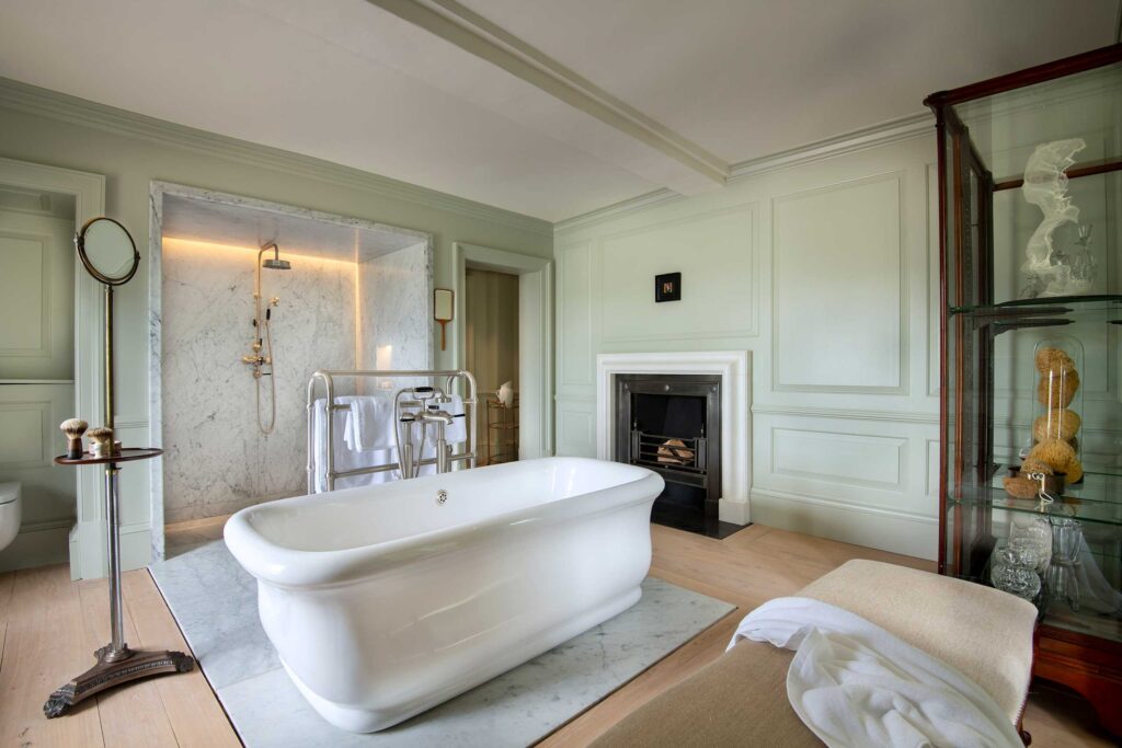 A freestanding white roll top bathtub in a large bathroom with pistachio coloured walls at The Newt in Somerset, Bruton, United Kingdom