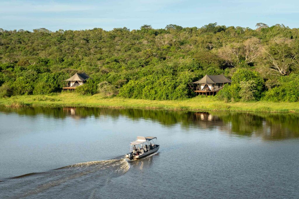 A boat nears the shore off two tented accommodations at Wilderness Magashi Camp in Akagera National Park, Rwanda