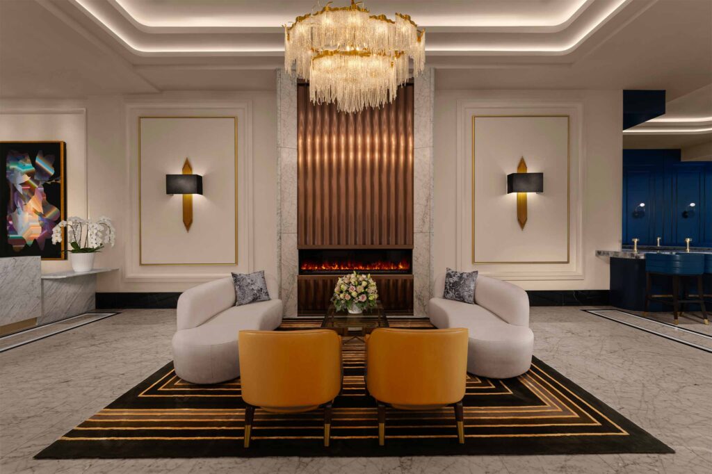 A contemporary chandelier hangs above a seating area with low couches in front of a recessed gas fireplace inside the lobby at AZUR Legacy Collection Hotel, Vancouver, Canada