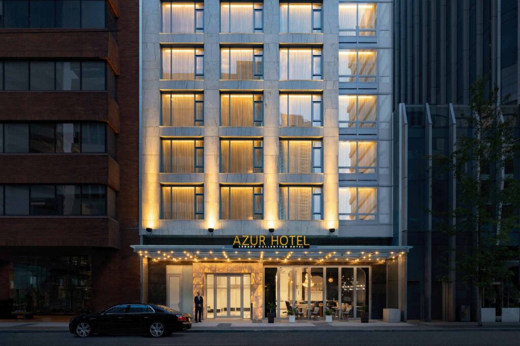 A black limousine in front of the spotlit facade with large windows at AZUR Legacy Collection Hotel, Vancouver, Canada