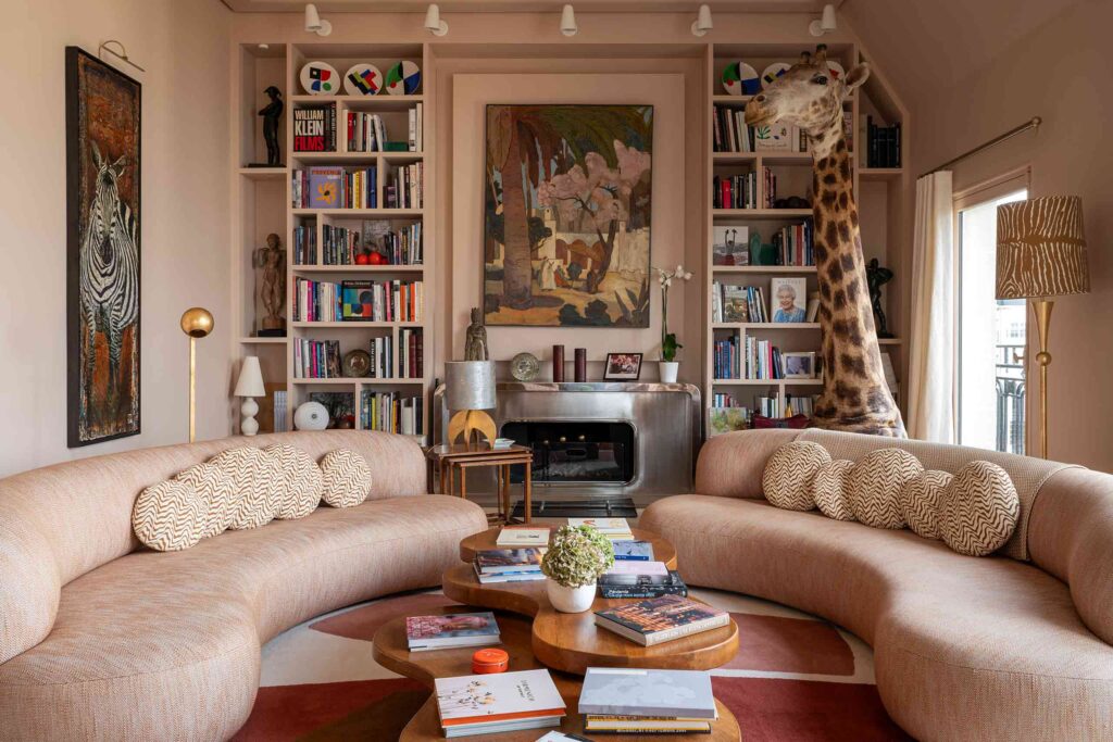An eclectic living room with a life-size giraffe sculpture, a silver fireplace, large artworks and curved sofas, inside a property in the portfolio of Le Collectionist by Max Aniort