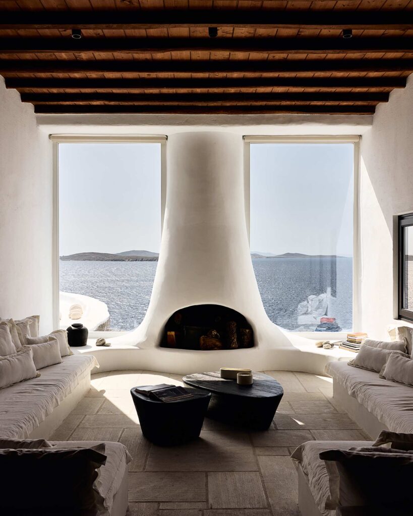 A whitewashed fireplace between two floor-to-ceiling windows offering views of the sea at Villa Lumina, a property in the portfolio of Le Collectionist by Max Aniort