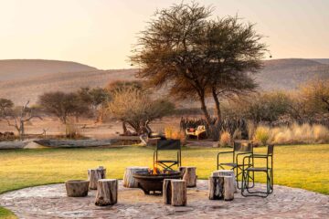 Seats around a log fire, with the bush in the background, at Okonjima Luxury Bush Camp, Okonjima Nature Reserve, Namibia