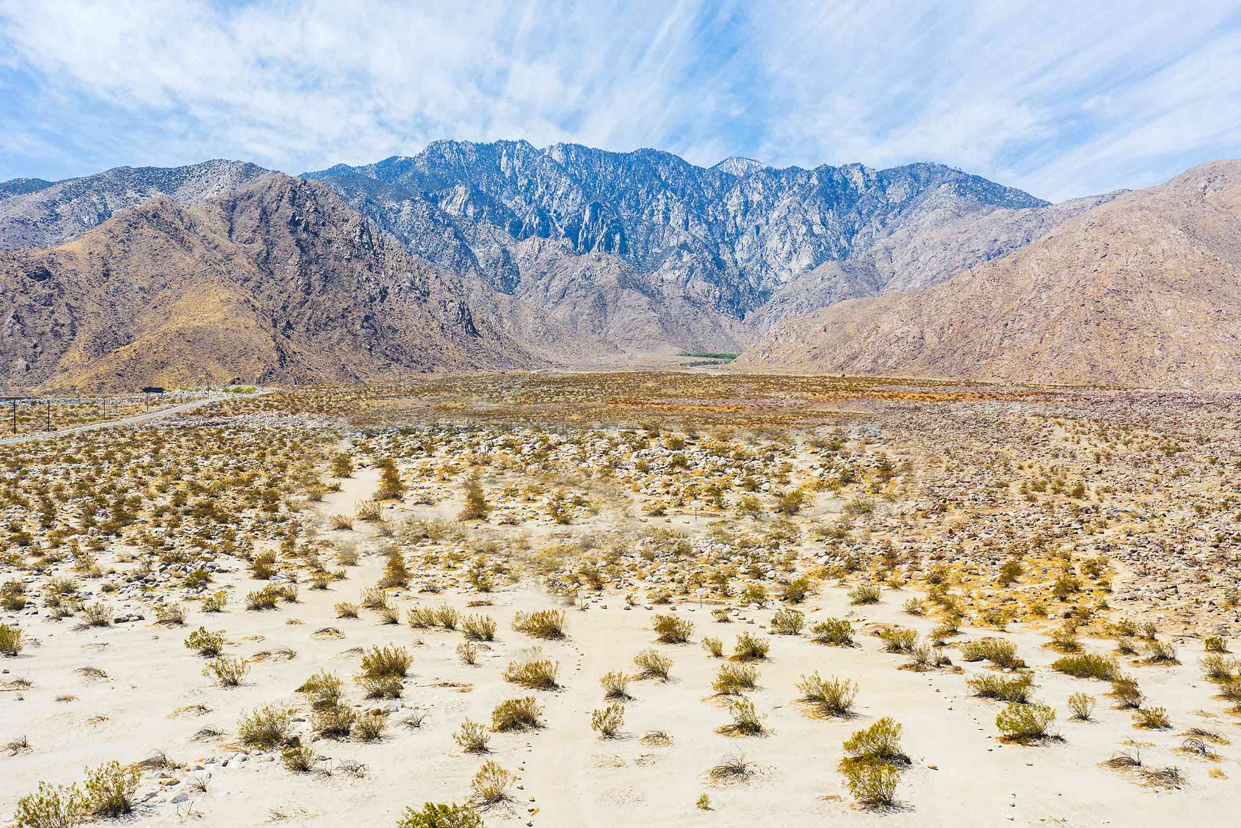 Panorama of the Coachella valley, with sandy desert and shrubs in the foreground and mountain range in the background