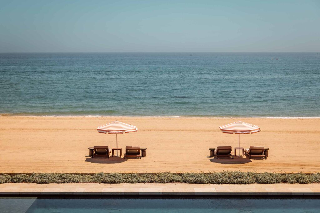 Four loungers beneath striped parasols sit on golden sand with a view of the Mediterranean Sea in Northern Morocco