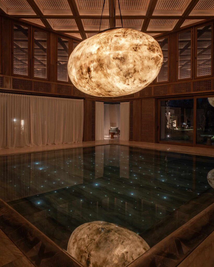 An oval-shaped, moon-inspired light fixture hangs above a pool in which small lights twinkle, Royal Mansour Tamuda Bay, Tamuda Bay, Morocco