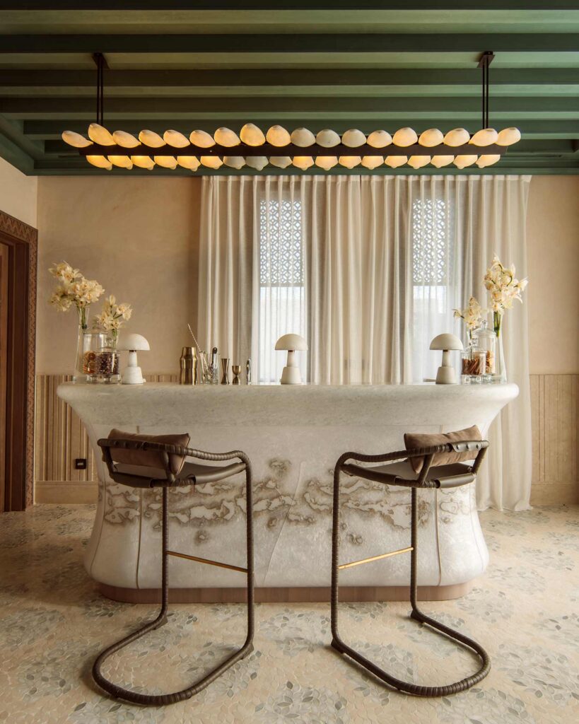 Two chairs in front of a white marble juice bar above which a modern light fixture hangs from a wooden, green ceiling, Royal Mansour Tamuda Bay, Tamuda Bay, Morocco