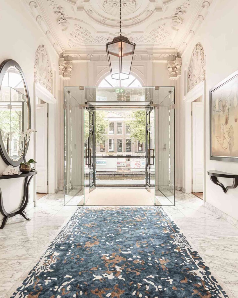 Entrance hallway of the Waldorf Astoria Amsterdam, with patterned blue carpet and glass and contemporary flourishes