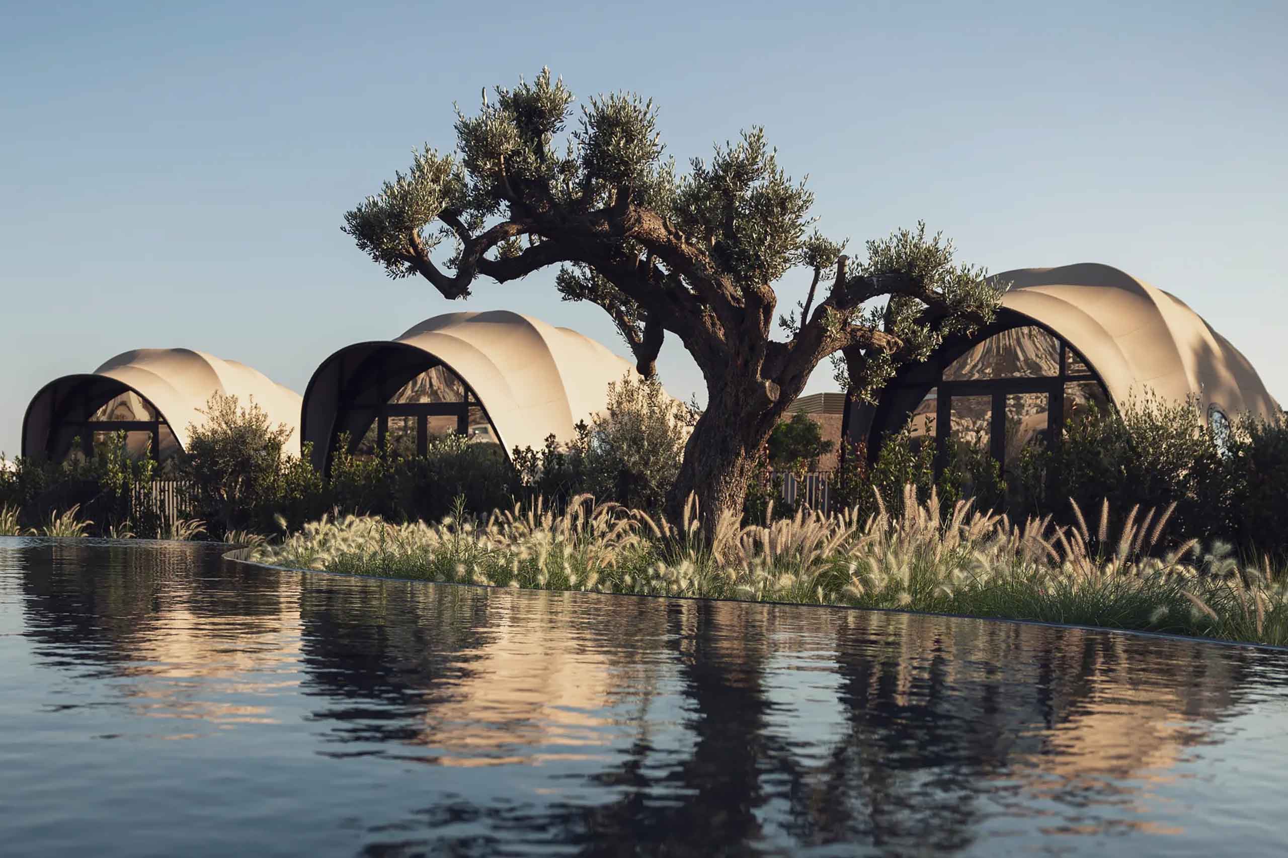 Three domed, sea-shell-like tented villas, or Luxtents overlook a man-made lagoon at 91 Athens Riviera, while a gnarly olive tree stands sentry out front of them