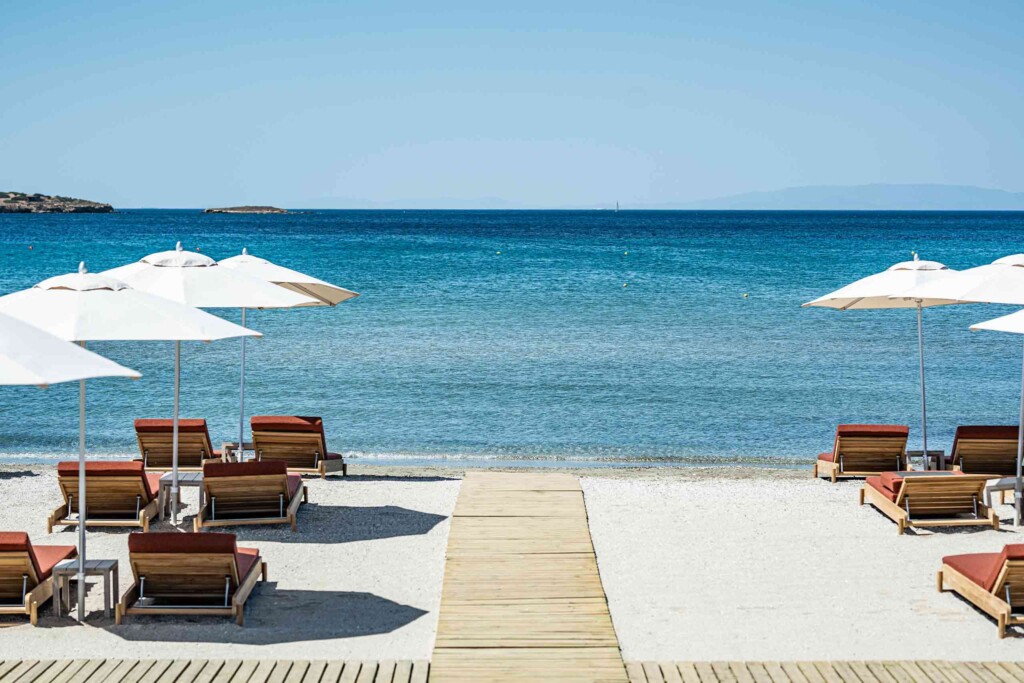 Red deck chairs at Barbarossa Beach club, next to 91 Athens Riviera look out to sea, white parasols dot the landscape