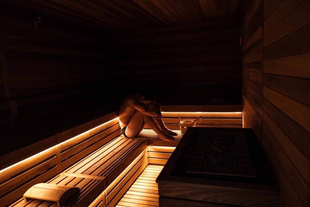 A man curls up, sitting in a sauna at Soma Spa – The Finest