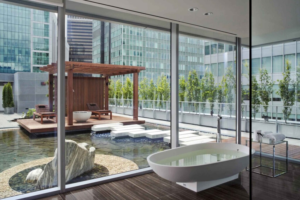 An egg-shaped bathtub in front of a glass wall offering a view of an adjacent, overwater walkway to a private pavilion, the Chairman's Suite at Fairmont Pacific Rim, Vancouver, Canada