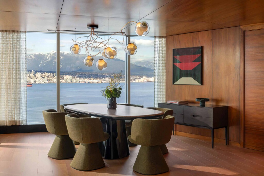Six moss green armchairs with retro design sit around a table beneath a Bocci pendant light in front of a glass wall offering views of the surrounding natural environment at Fairmont Pacific Rim, Vancouver, Canada