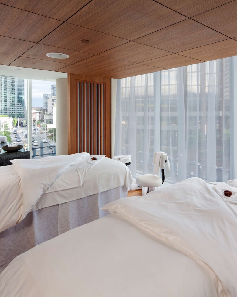 Two massage tables draped in white linen stand next to one another in front of glass walls offering urban views at Fairmont Pacific Rim, Vancouver, Canada