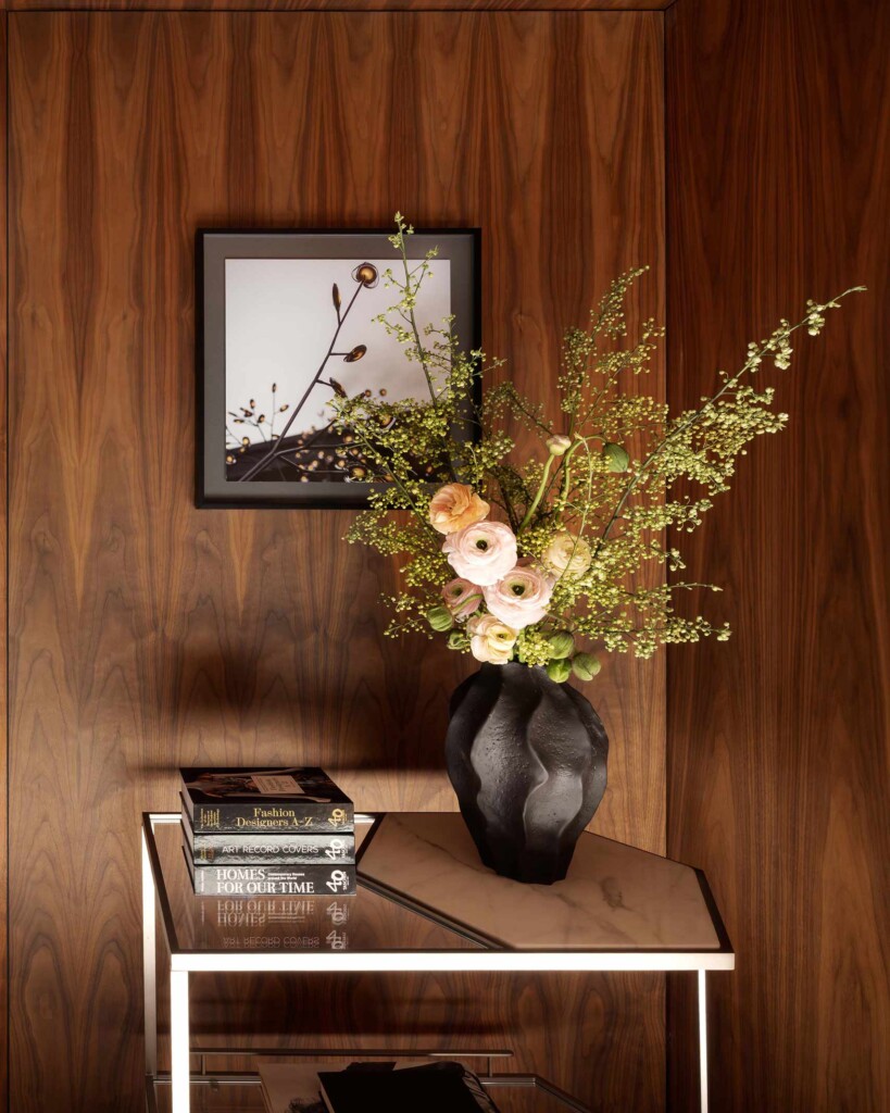 A minimalist flower bouquet in a vase stands on a small table next to a pile of books