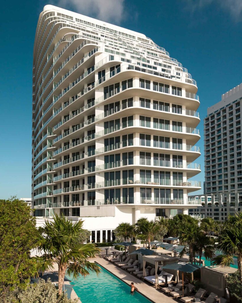 Exterior architecture of the Four Seasons Hotel and Residences Fort Lauderdale. It represents a ship-like, white tower. Down below, a man relaxes in one of two swimming pools