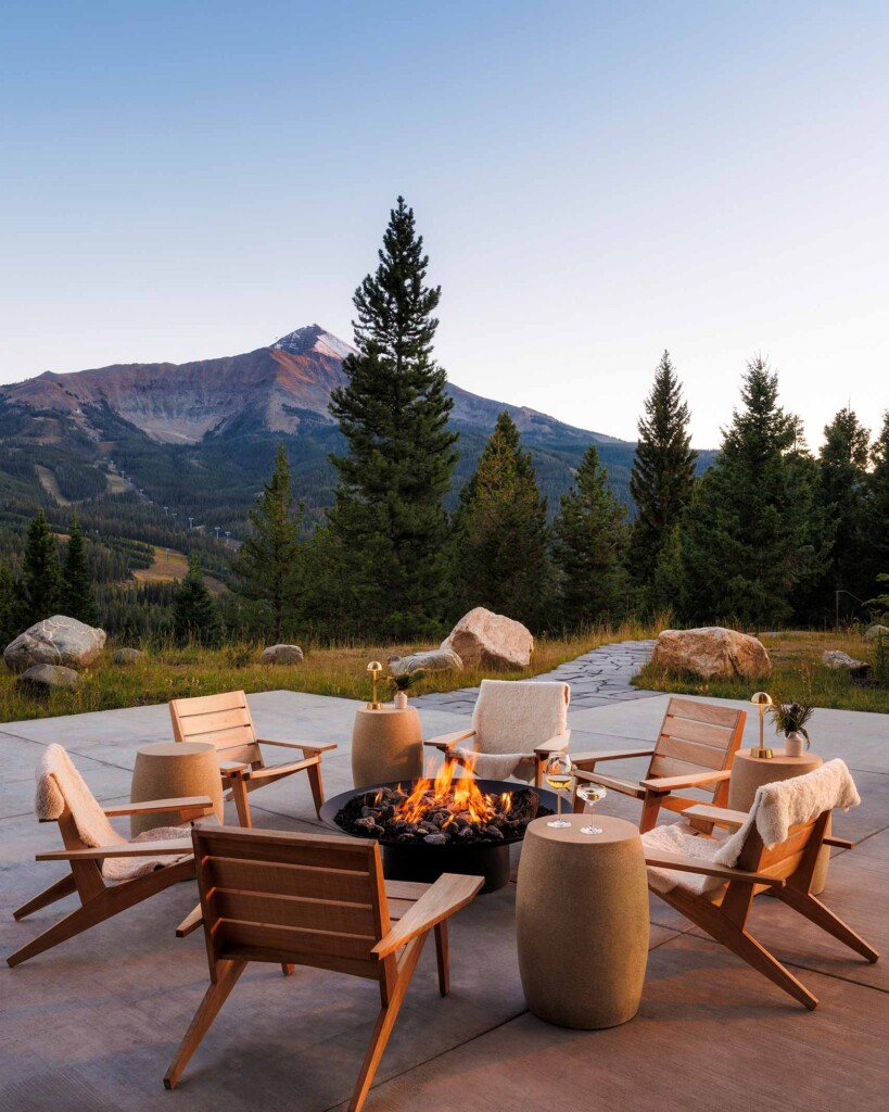 Armchairs surround a log fire as the sun sets over the mountains of Big Sky, Montana