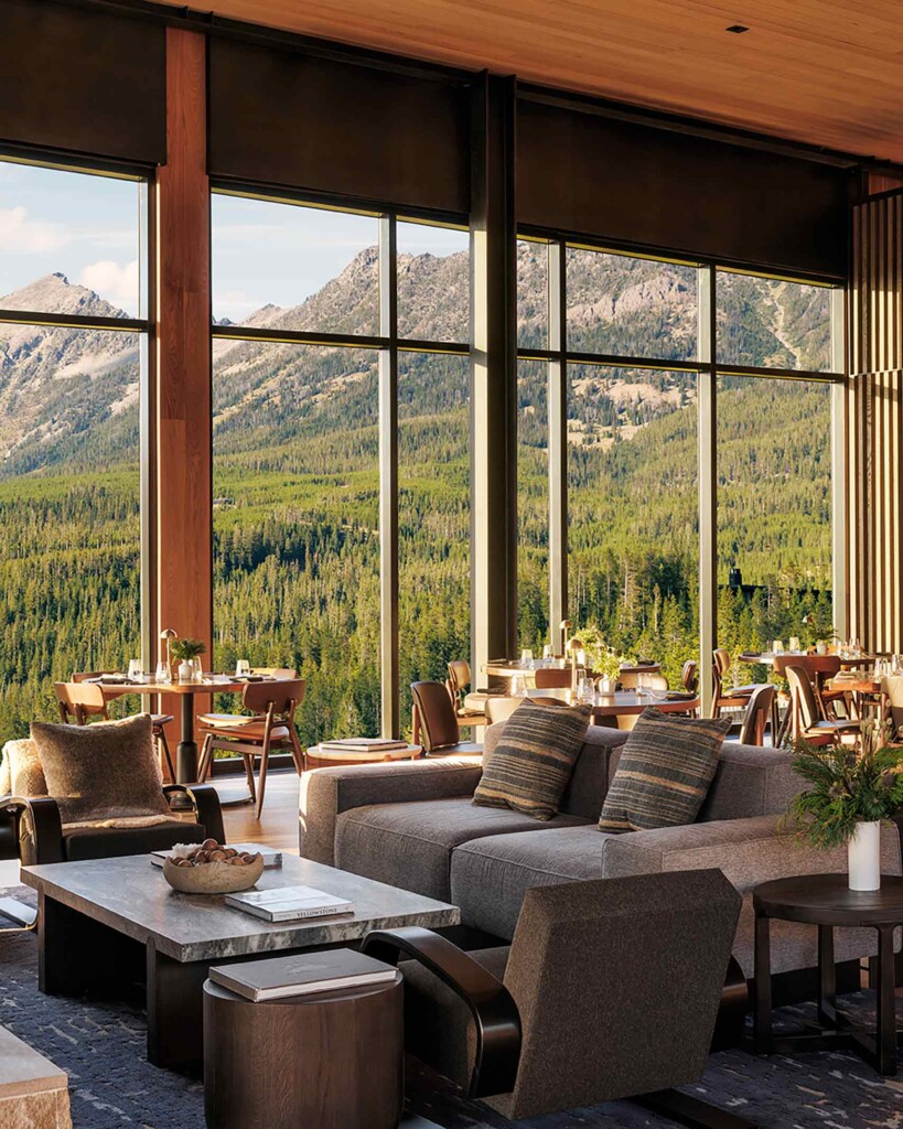A cosy seating arrangement and tables set for lunch in front of floor-to-ceiling windows offering views of the surrounding mountains at One&Only Moonlight Basin, Big Sky, Montana, USA