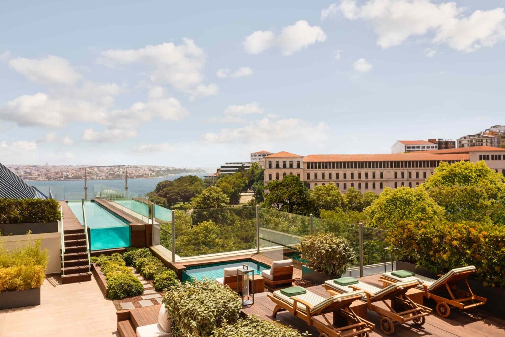 Three sun loungers surrounded by bushes are situated in front of a jacuzzi and an outdoor infinity swimming pool with a view of the Bosphorus at The Ritz-Carlton, Istanbul, Türkiye