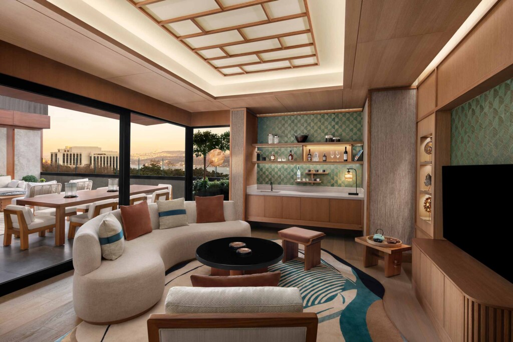A spacious lounging and TV area with a couch and and a wet bar at its end in front of a glass windows offering a view of the Bosphorus, inside the Nobu Suite