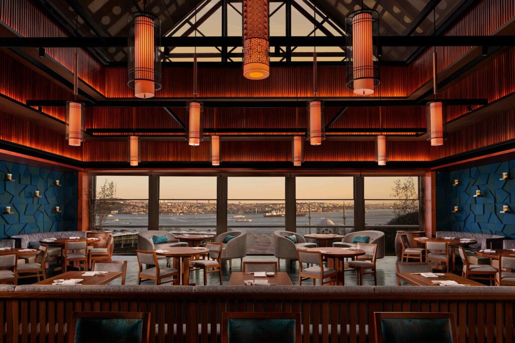 Japanese-inspired pendant lights hang from the ceiling above seating arrangements in front of a view of the Bosphorus at Nobu Restaurant