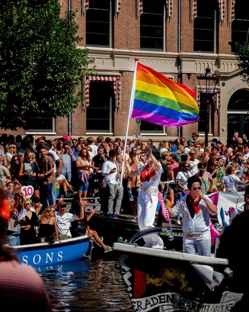 Party goers raise a rainbow flag from a boat on a canal during Pride