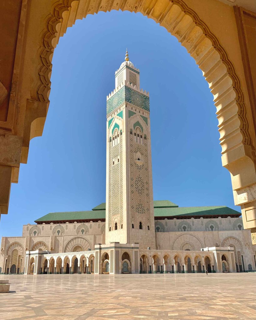 A mosque minaret in green and white, framed in an arabesque archway in Casablanca, Morocco