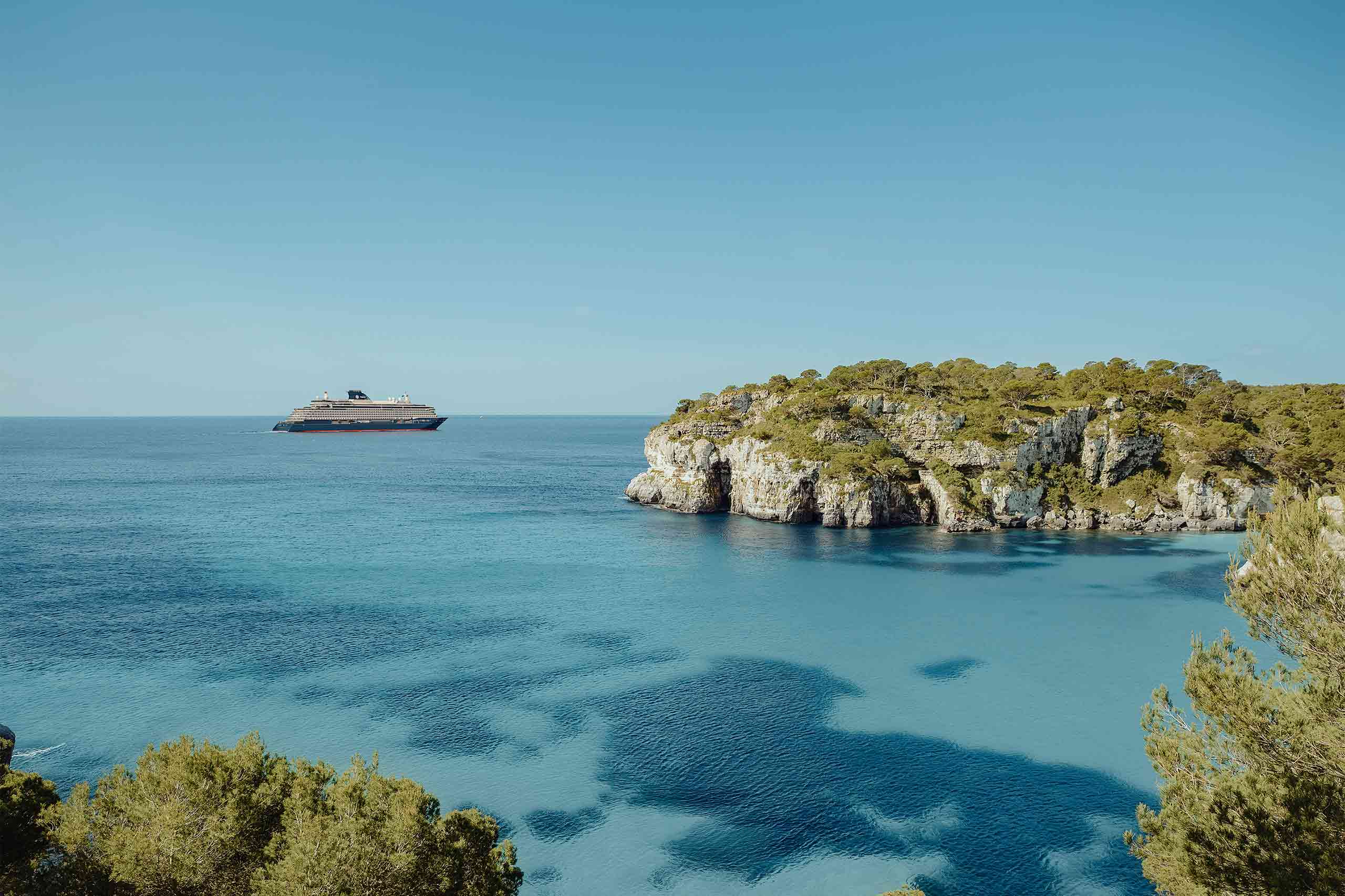 Explora Journeys ship on a turquoise sea in the background with Mediterranean islands in the foreground