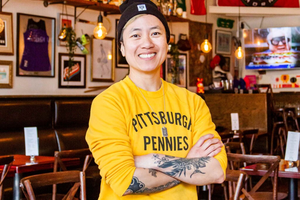 Wearing a yellow long-sleeve shirt and a dog tag around her neck, Jenny Nguyen smiles for the camera at The Sports Bra, Portland, Oregon, USA