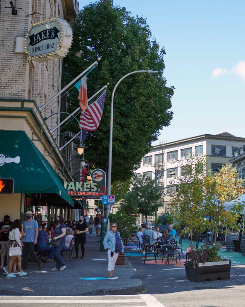 A street corner in Portland, Oregon, with trees dominating the urban landscape and people going about their days in the foreground