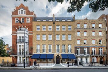The hotel's elegant Georgian townhouse façade features honey-coloured brickwork, navy awnings, tall sash windows, and a central entrance overlooking a quiet Chelsea street.