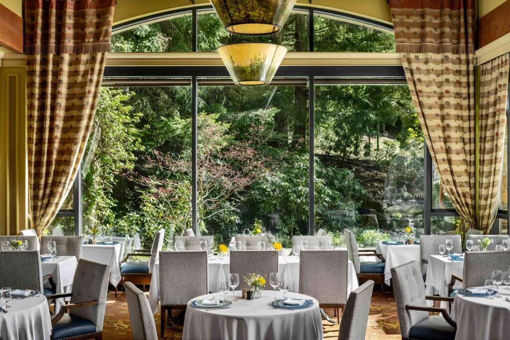 Lunch tables decked in white tablecloths are set in front of a large window offering a view into the adjoining forest, Wildflower Restaurant, Canada