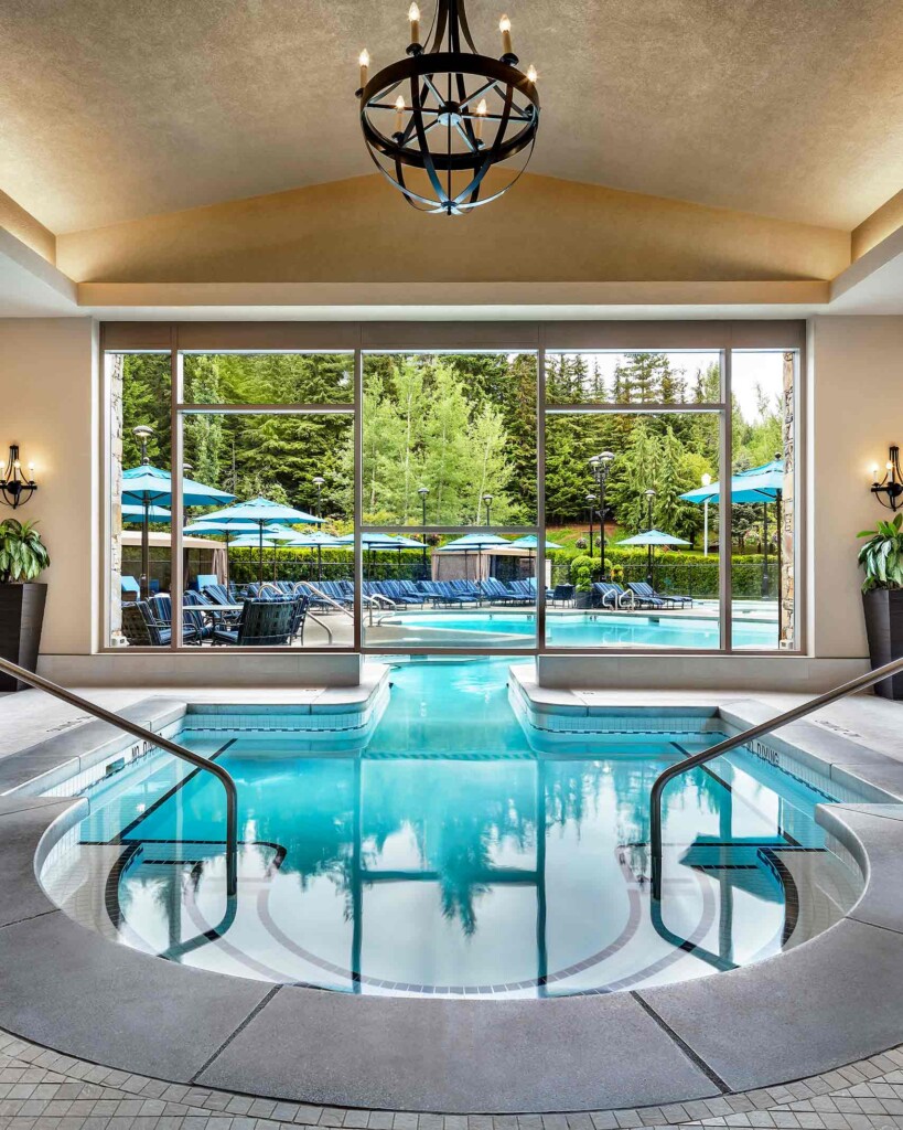 Stairs lead down into a large indoor-outdoor pool beneath a golden, arched ceiling and with a window offering a view of the surrounding natural landscape, Vida Spa, Canada