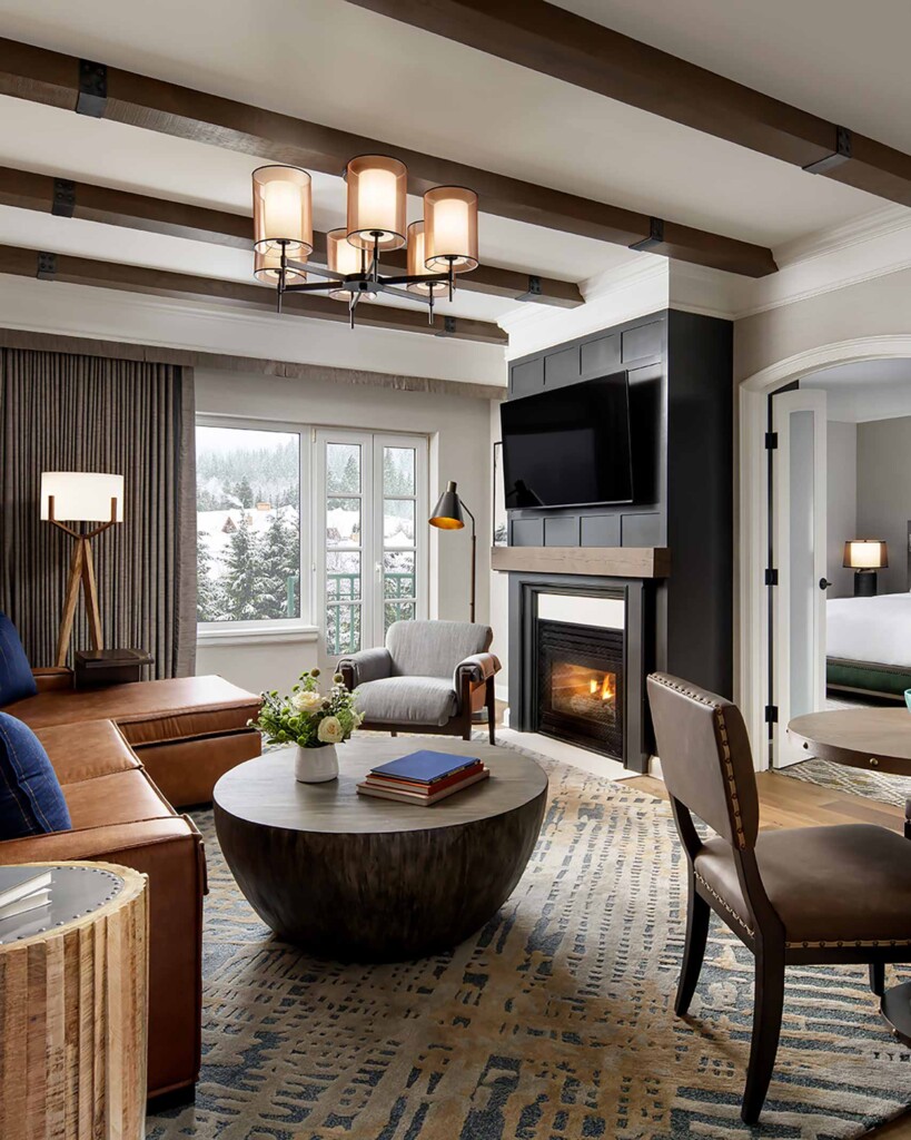 A suite will Alpine-inspired interiors, fresh flowers, and an exposed wood-beamed ceiling as well as a view of a snowy landscape at Fairmont Chateau Whistler, Whistler, Canada