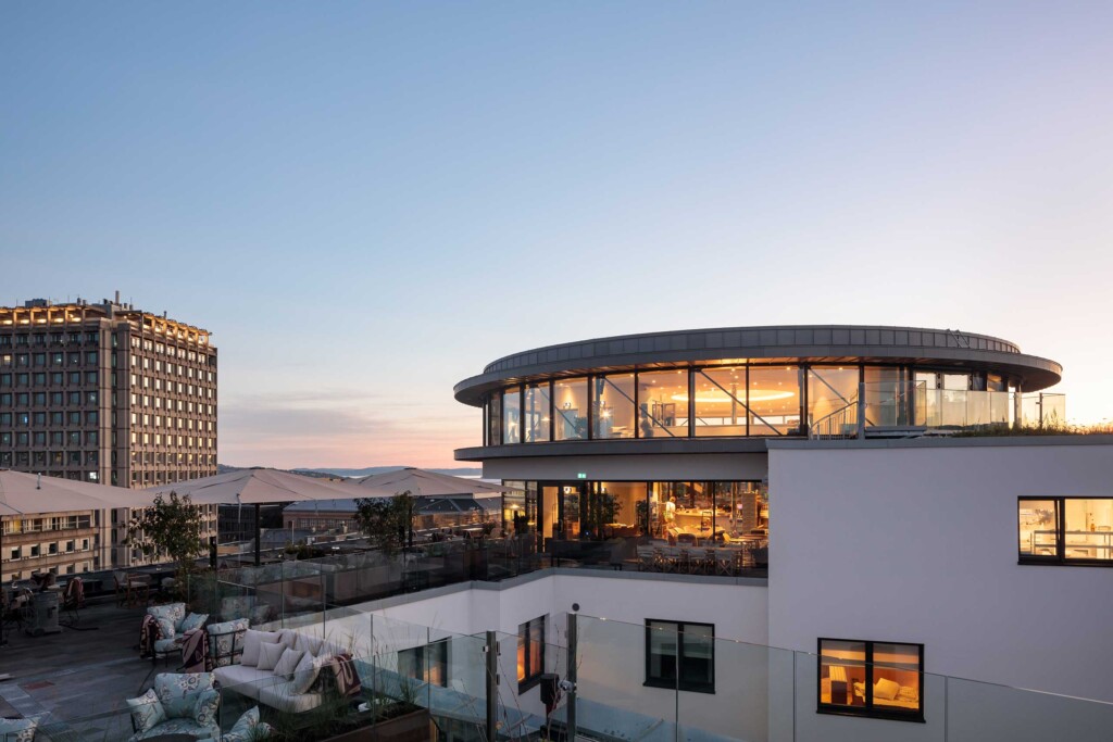 A circular, glass-encased restaurant and bar sits atop a modern, white building as the sun sets over Oslo, Sommerro, Oslo, Norway