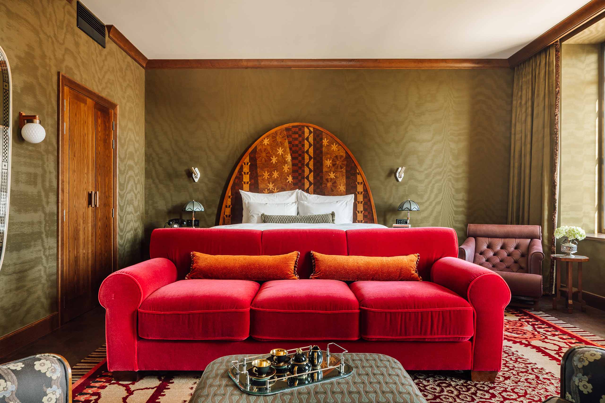 A bright red sofa at the foot of a bed in a luxurious suite held in khaki and brown tones, Sommerro, Oslo, Norway